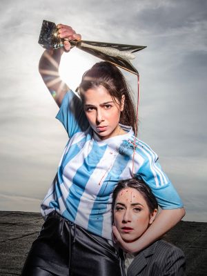 Auf dem Foto sind zwei junge Schauspielerinnen zu  sehen. Die linke Frau trägt ein gestreiftes Trikot und recht einen Pokal über ihren Kopf empor. Ihr Gesichtsausdruck ist grimmig. Sie hält den Kopf der anderen Person im Schwitzkasten. Auf das Gesicht der zweiten Frau tropft Blut aus dem Pokal herab.